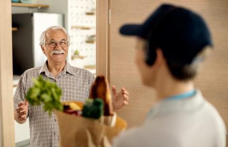 Happy senior man talking to deliverer who is brining him bag with groceries at home.